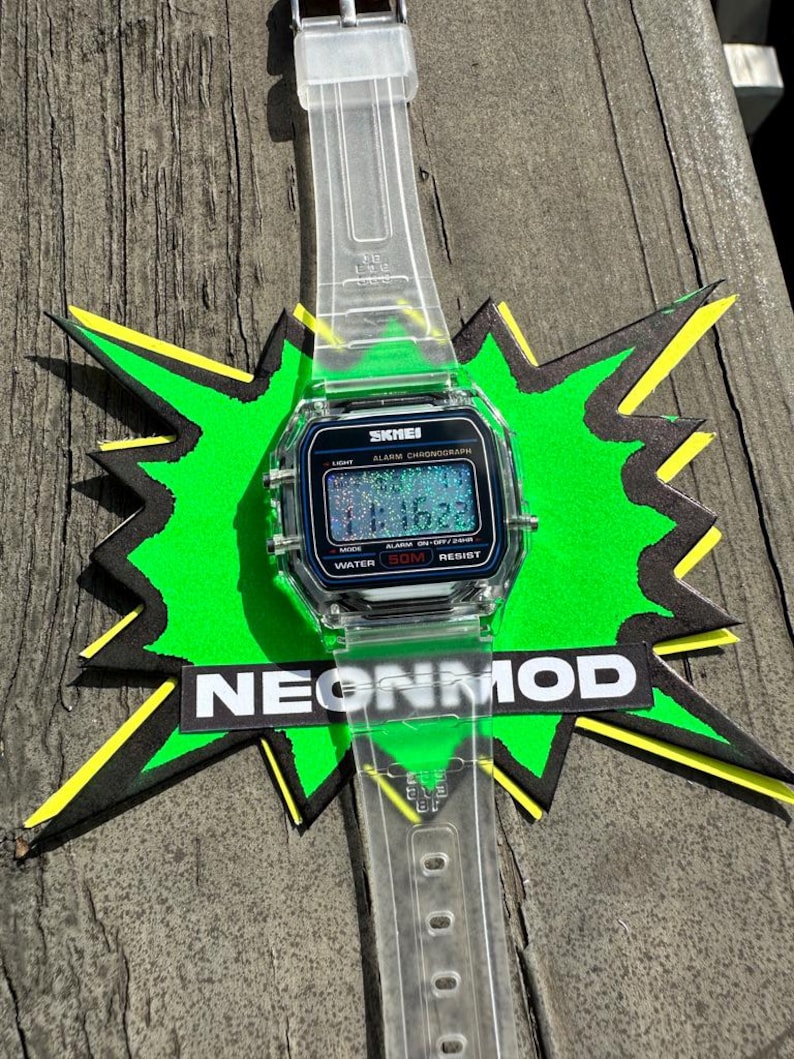 May include: A digital wristwatch with a clear, transparent resin strap and a square case. The watch face features the brand name SKMEI, the text ALARM CHRONOGRAPH, and WATER 50M RESIST. The digital display shows the time 11:16 with a glittery effect.