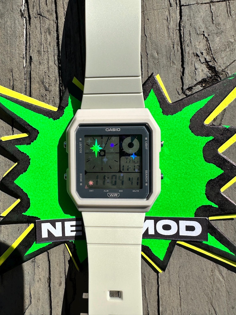 Pu&ograve; includere: Un orologio da polso digitale color bianco sporco opaco con cassa quadrata e cinturino in resina abbinato. Il quadrante presenta il logo Casio, un display digitale con icone a forma di stella e la scritta WR. Mostra l'ora 11:04 e il giorno THU.