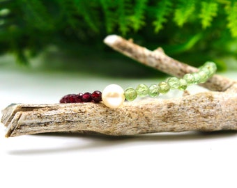 Puede incluir: Un brazalete hecho con cuentas verdes, rojas y blancas. El brazalete está hecho con cuentas pequeñas y redondas y una cuenta de perla blanca más grande.