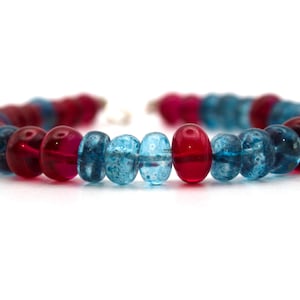 Peut inclure: Un bracelet composé de perles de verre bleues et rouges. Les perles sont rondes et ont une surface légèrement texturée.