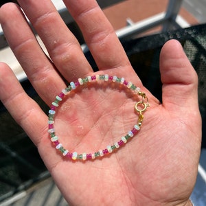 Può includere: Un braccialetto delicato realizzato con piccole perline rotonde in tonalità di bianco, verde e rosa. Il braccialetto ha una chiusura dorata.