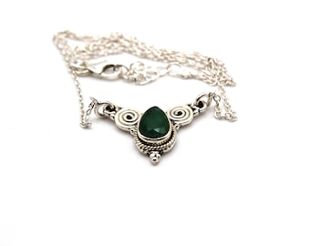 May include: A silver necklace with a green gemstone pendant. The pendant is surrounded by intricate silver designs.