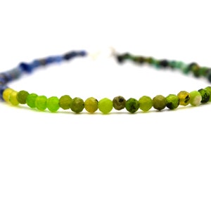 May include: A multi-colored beaded necklace with blue, green, and yellow beads. The beads are faceted and have a slightly irregular shape.