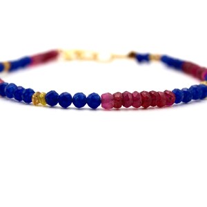 Può includere: Un braccialetto di pietre preziose blu e rosse con accenti dorati. Il braccialetto è fatto di piccole perline rotonde.