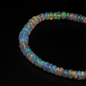 May include: A strand of iridescent opal beads in a light blue, white, and pink color palette. The beads are strung together to form a necklace or bracelet.
