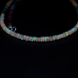 Può includere: Una collana delicata realizzata con piccole perle di opale iridescente. Le perle sono infilate su una catena d'argento e hanno un sottile bagliore arcobaleno.