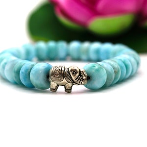Könnte beinhalten: Ein hellblaues Edelstein-Armband mit einem silbernen Elefanten-Anhänger. Das Armband besteht aus runden Perlen und ist auf einem Gummiband gefädelt.
