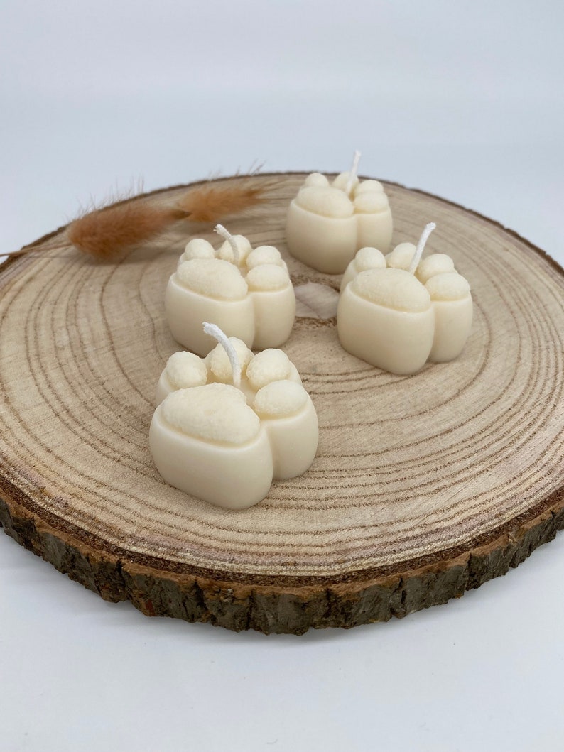 May include: Four white paw print shaped candles on a wooden slice. The candles are made of wax and have a white wick.