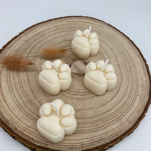 May include: Four white paw print shaped candles on a wooden slice. The candles have a white wick.