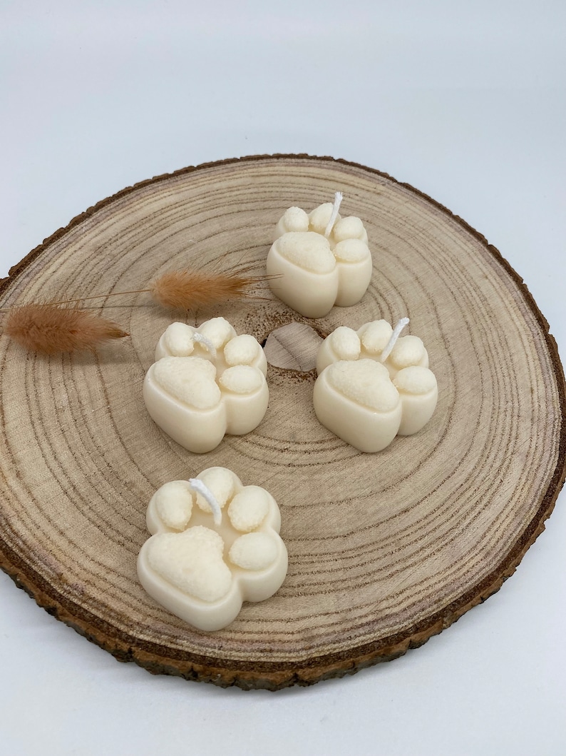 May include: Four white paw print shaped candles on a wooden slice. The candles have a white wick.