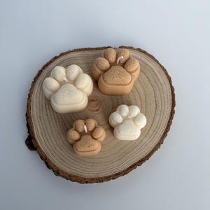 May include: Four paw print shaped candles on a wooden slice. Two candles are beige and two are white.