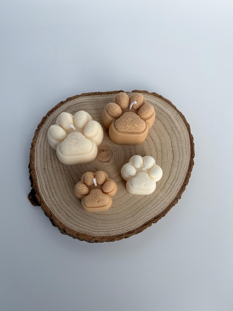 May include: Four paw print shaped candles on a wooden slice. Two candles are beige and two are white.