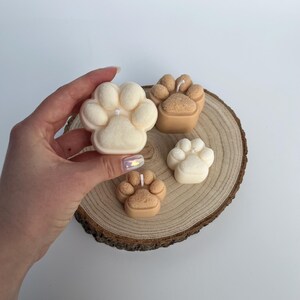 May include: Four paw print shaped candles, two are white and two are brown, on a wooden slice.