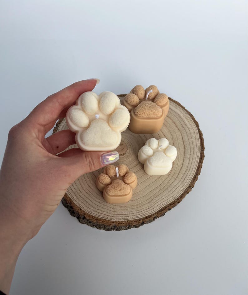 May include: Four paw print shaped candles, two are white and two are brown, on a wooden slice.