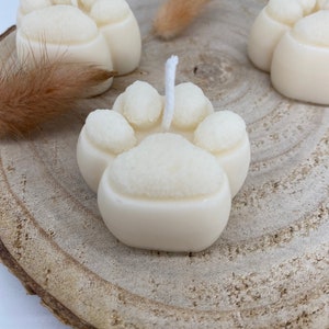 May include: Three white paw print shaped candles on a wooden slice. Each candle has a white wick.