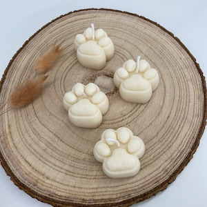 May include: Four white paw print candles on a wooden slice. The candles are made of a textured wax and have a white wick.