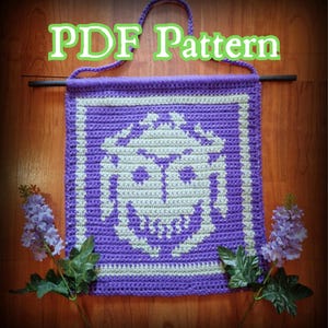 Könnte beinhalten: Ein gehäkeltes Wandbehang in Lila und Creme mit einem geometrischen Design. Der Text "PDF Pattern" wird oben angezeigt. Der Behang wird an einem Holzstab aufgehängt und hat eine lila Schlaufe zum Aufhängen.