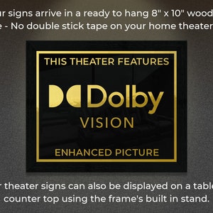 May include: A black framed sign with gold lettering that reads "This Theater Features Dolby Vision Enhanced Picture". The sign is 8 inches by 10 inches and is ready to hang on a wall.