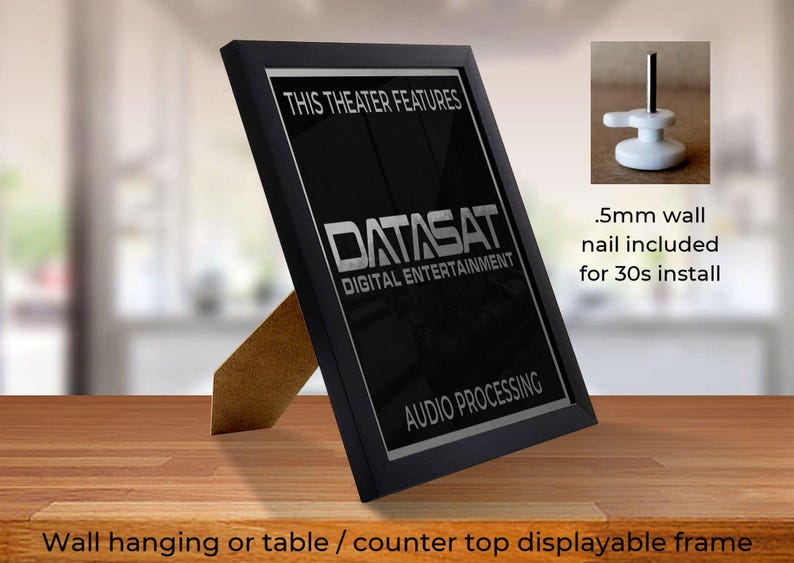 May include: A black framed sign with the text "THIS THEATER FEATURES DATASAT DIGITAL ENTERTAINMENT AUDIO PROCESSING". The sign is displayed on a wooden surface and includes a small wall nail for installation.
