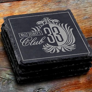 May include: A set of black slate coasters with a silver design featuring the text "Walt Disney's Club 33".