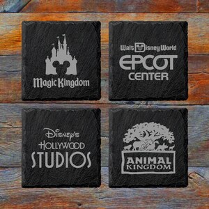 May include: Four black slate coasters with white text and images. The coasters feature the names of the four theme parks at Walt Disney World: Magic Kingdom, Epcot Center, Disney's Hollywood Studios, and Animal Kingdom.
