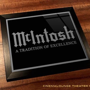 Pode incluir: Um sinal enquadrado em preto com fundo prateado e texto branco. O texto diz "McIntosh" em uma fonte estilizada e "A Tradition of Excellence" em uma fonte menor.