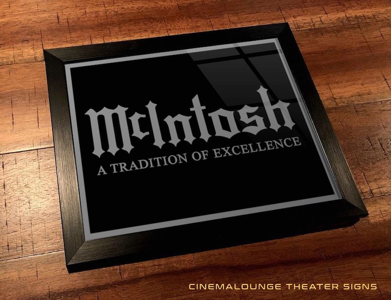 Pode incluir: Um sinal enquadrado em preto com fundo prateado e texto branco. O texto diz "McIntosh" em uma fonte estilizada e "A Tradition of Excellence" em uma fonte menor.