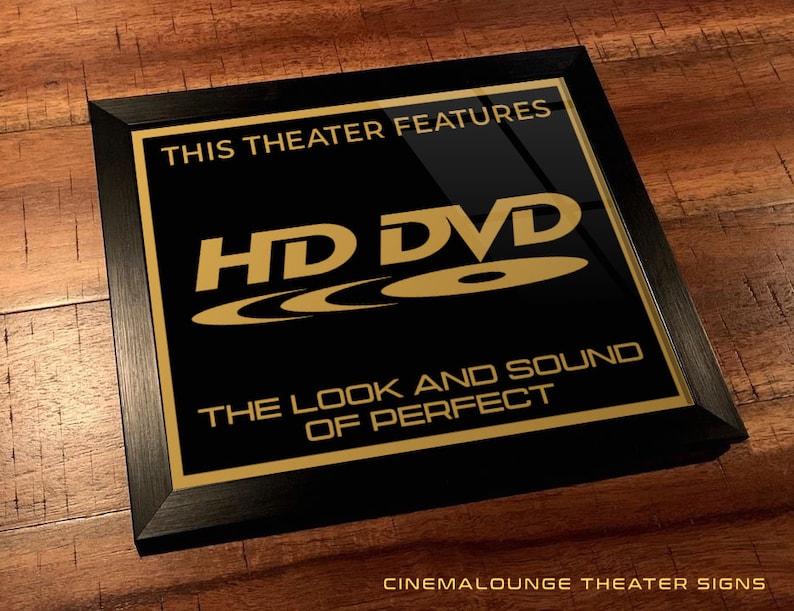 May include: Black framed sign with gold text that reads "This theater features HD DVD - The look and sound of perfect."  The sign also includes the HD DVD logo.  The sign is on a wood background.  Cinemalounge Theater Signs.