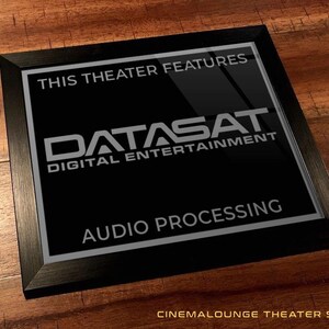 May include: A black framed sign with the text "THIS THEATER FEATURES DATASAT DIGITAL ENTERTAINMENT AUDIO PROCESSING." The sign is on a wooden surface. The sign is a cinema lounge theater sign.