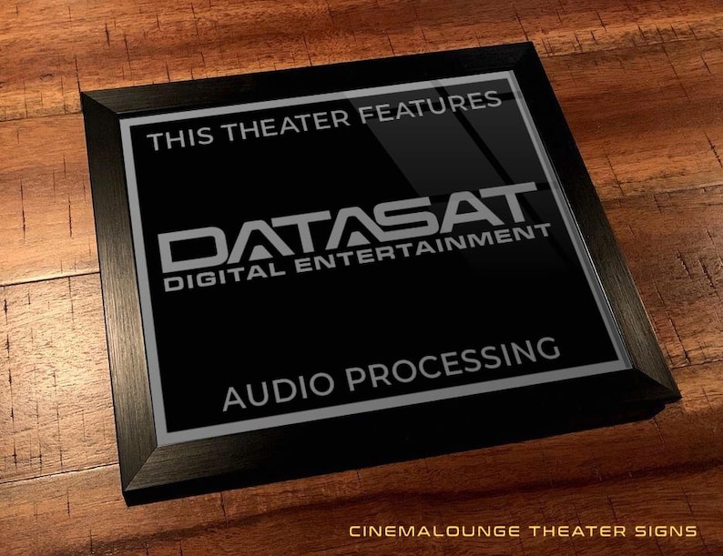 May include: A black framed sign with the text "THIS THEATER FEATURES DATASAT DIGITAL ENTERTAINMENT AUDIO PROCESSING." The sign is on a wooden surface. The sign is a cinema lounge theater sign.
