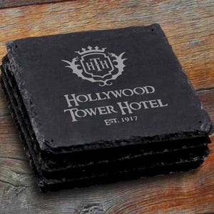 May include: Set of four black slate coasters featuring a gray engraved logo for the Hollywood Tower Hotel with the text "Hollywood Tower Hotel Est. 1917".