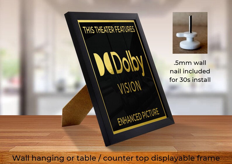 May include: Black framed sign with gold lettering that reads "This Theater Features Dolby Vision Enhanced Picture". The sign is on a wooden table and has a small easel stand.