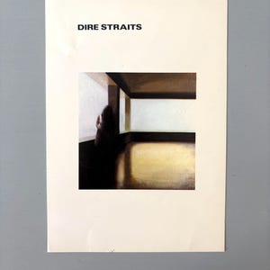 May include: A rectangular white paper print featuring the black text DIRE STRAITS at the top. Below the text is a square image depicting a dark silhouette of a person standing in a room with a large window, light walls, and a golden floor.