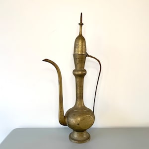 May include: A vintage brass teapot with an ornate design and a tall spout. The teapot has a lid with a finial and a handle.
