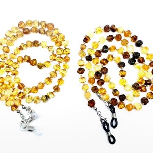 May include: Two amber beaded eyeglass chains. One chain is a mix of yellow and brown beads, the other is a mix of yellow, brown, and black beads. Each chain has silver-colored clasps to attach to glasses.