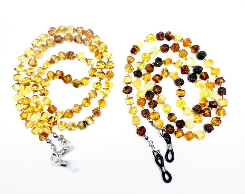 May include: Two amber beaded eyeglass chains. One chain is a mix of yellow and brown beads, the other is a mix of yellow, brown, and black beads. Each chain has silver-colored clasps to attach to glasses.