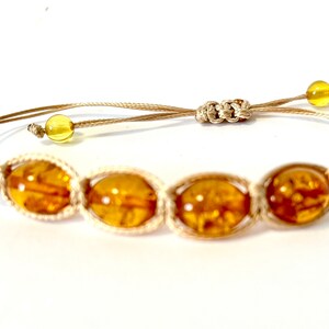 Pode incluir: Um bracelete de macram&eacute; bege com quatro contas ovais de &acirc;mbar.