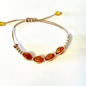 Pode incluir: Um bracelete de cord&atilde;o marrom com quatro contas de &acirc;mbar. O bracelete &eacute; ajust&aacute;vel com um n&oacute; deslizante.