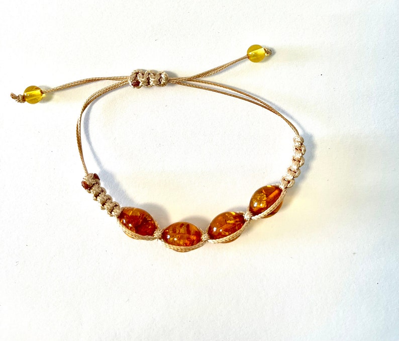 Pode incluir: Um bracelete de cord&atilde;o marrom com quatro contas de &acirc;mbar. O bracelete &eacute; ajust&aacute;vel com um n&oacute; deslizante.