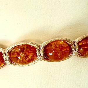 Pode incluir: Close-up de um bracelete de &acirc;mbar marrom com cord&atilde;o branco. As contas s&atilde;o ovais e t&ecirc;m um aspecto natural e org&acirc;nico.