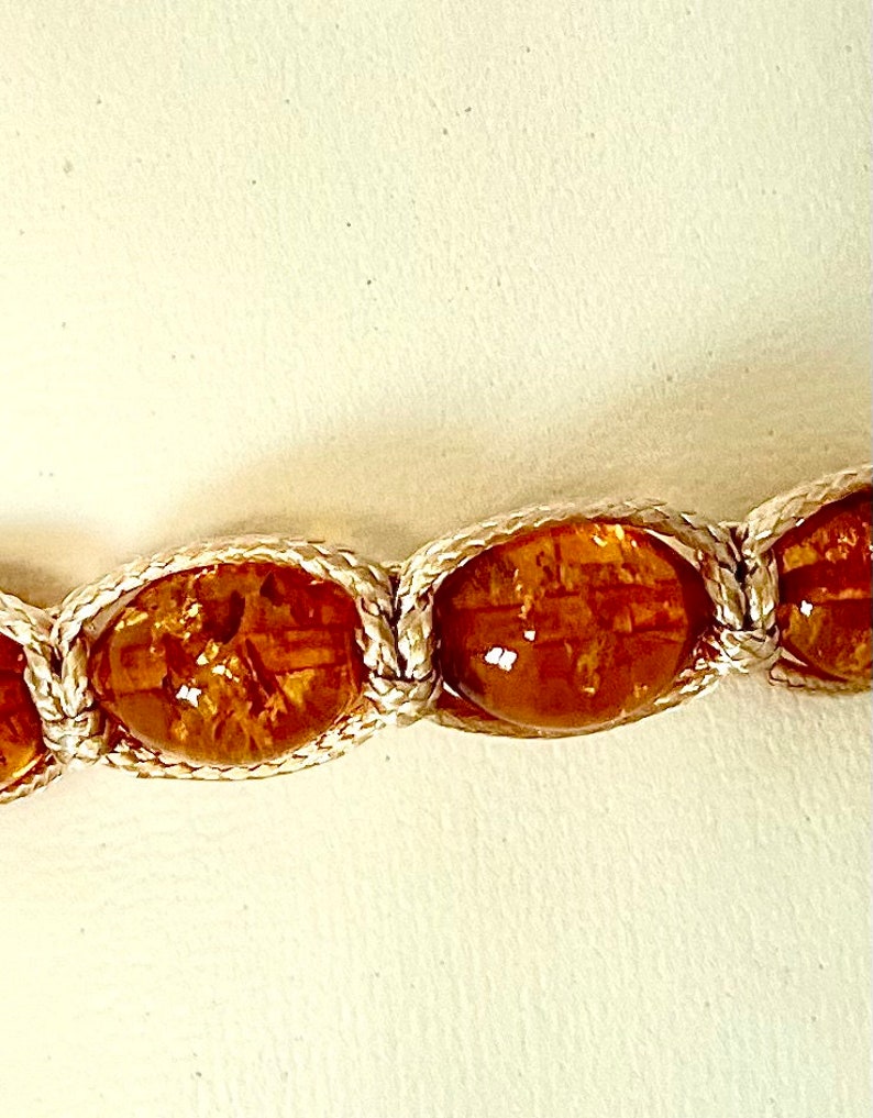 Pode incluir: Close-up de um bracelete de &acirc;mbar marrom com cord&atilde;o branco. As contas s&atilde;o ovais e t&ecirc;m um aspecto natural e org&acirc;nico.