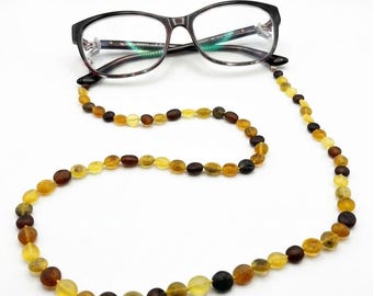 May include: A pair of dark tortoiseshell eyeglasses attached to a long beaded chain. The chain consists of smooth, round, translucent beads in varying shades of yellow, orange, and dark brown, creating a multi-colored amber-like appearance.