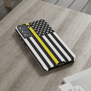 May include: A black and white phone case with a thin yellow stripe across the middle, featuring a design of the American flag. The case has a cutout for the phone's camera lens.