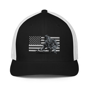 May include: A black and white trucker hat with a white mesh back. The front of the hat features an embroidered image of a welder working on a metal surface in front of an American flag.