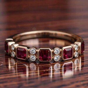 Puede incluir: Un anillo de oro rosa con un patrón repetitivo de rubíes rojos de corte cuadrado que se alternan con pares de pequeños diamantes blancos redondos. Las piedras preciosas están engastadas en bisel a lo largo de la mitad superior del anillo.