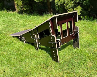 May include: A wooden ramp structure with a dark finish, featuring a sloped surface and a series of rectangular openings. The ramp is secured with black cords and is set on a grassy lawn, suggesting outdoor use.