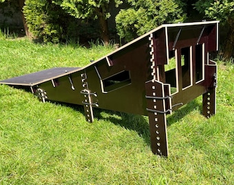 May include: A brown wooden ramp structure with a flat top and angled sides, designed for outdoor use. The ramp is constructed with multiple wooden pieces and secured with black rubber bands. It is set on a grassy surface.