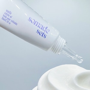 Puede incluir: Un tubo transparente con una etiqueta morada que dice "somade sets" y "vanilla cuticle oil, huile pour cuticules, 10ml/0.3fl oz". El tubo tiene una punta de gotero transparente y está dispensando un líquido transparente.