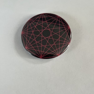 Op de afbeelding: Een zwarte knoop met een rood geometrisch ontwerp. Het ontwerp is een reeks van elkaar kruisende lijnen die een stervormig patroon vormen.