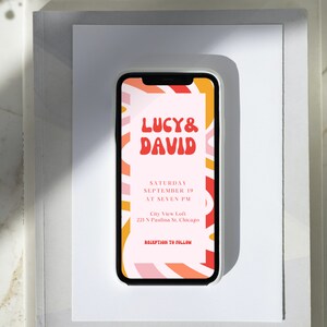 May include: A mobile phone screen displaying a wedding invitation with a colorful abstract background. The invitation reads "Lucy & David" in a red, bubbly font. The text below reads "Saturday, September 19 at Seven PM, City View Loft, 221 N Paulina St, Chicago, Reception to Follow."